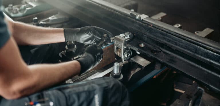 Eine Person in Arbeitskleidung und mit schwarzen Handschuhen führt im Rahmen der Bahntechnik gezielte Wartungs- oder Reparaturarbeiten an einem Abschnitt der Schieneninfrastruktur durch. Mithilfe spezialisierter Werkzeuge werden Metall- und Aluminiumkomponenten auf dem Gleis präzise ausgerichtet oder befestigt. Der Arbeitsbereich könnte Teil einer Reparatur an der Weiche sein, wobei die schwache Beleuchtung die industrielle Umgebung und die technische Komplexität der Bahnwartung unterstreicht. Solche Maßnahmen sind essenziell für die Sicherheit und Verfügbarkeit der Bahninfrastruktur.