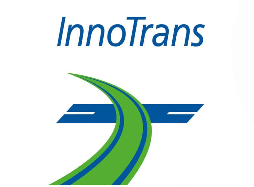 Das Bild zeigt das InnoTrans-Logo. Oben steht in blauer Schrift das Wort „InnoTrans“. Darunter befindet sich eine stilisierte Grafik eines grün-blauen Schienenstrangs oder Weges, der sich nach oben wölbt und ein dynamisches und futuristisches Design bildet, das die Innovation in der Schmiedeteile-Herstellung widerspiegelt.