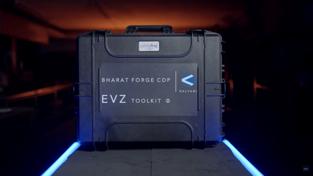 A black hard-shell case labeled "Bharat Forge CDP EVZ Toolkit by Kalyani" is displayed in a dimly lit industrial setting. The case, used in Schmiedeteile Automotive, features a "safetyBag" sticker on top and rests on a surface illuminated by blue lights.