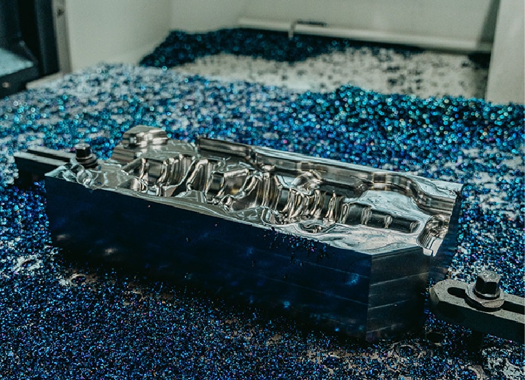 Eine glänzende, bearbeitete Metallform liegt umgeben von blauen Metallspänen auf einer Arbeitsfläche und reflektiert das Licht in einer industriellen Umgebung.