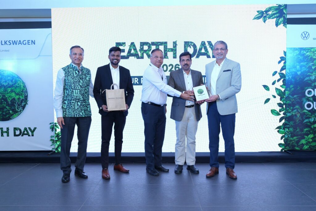 Fünf Männer in formeller Kleidung stehen auf einer Bühne während einer Veranstaltung zum Earth Day 2024. Drei Männer in der Mitte tauschen eine Plakette und eine Geschenktüte aus. Auf einer großen Leinwand hinter ihnen ist "EARTH DAY 2024" zu sehen und es sind Blätter zu sehen.