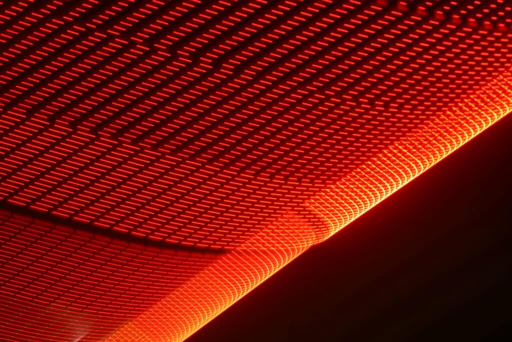 Nahaufnahme eines leuchtenden orange-roten LED-Gitters mit geschwungenen Linien und hellen Lichtern, das vor einem dunklen Hintergrund einen abstrakten, futuristischen Eindruck vermittelt. Steht für Weichenheizung.